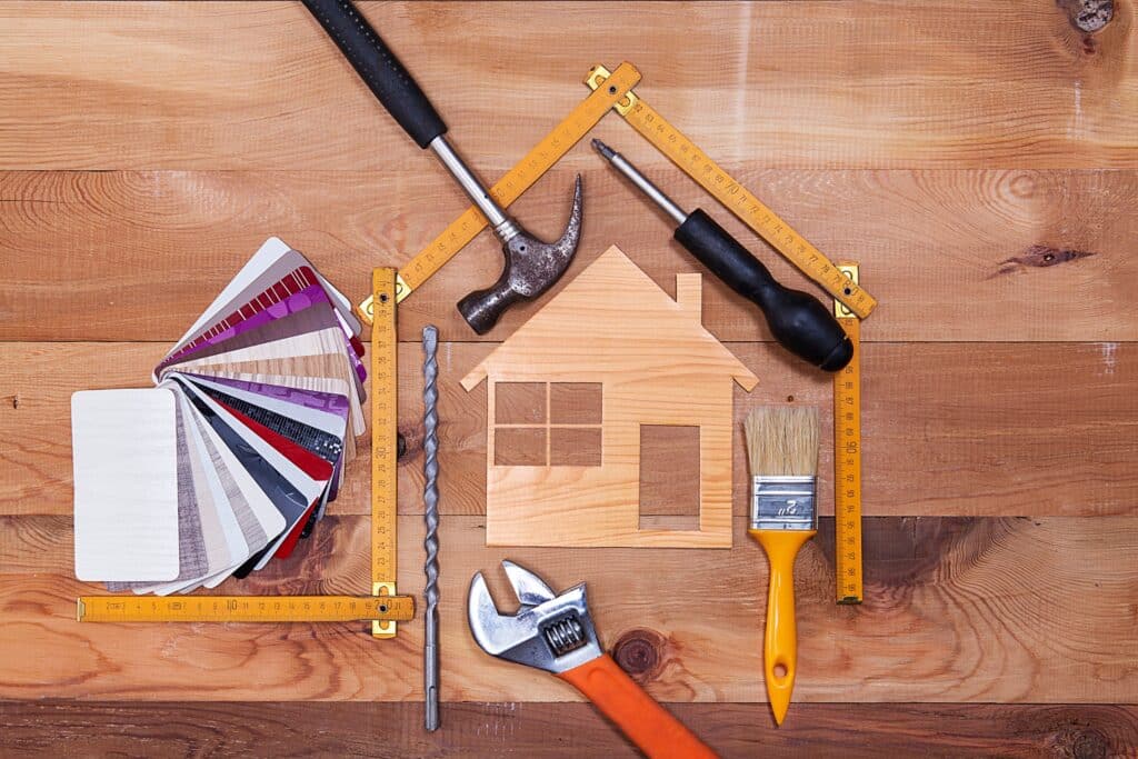 Des palettes de couleurs, une règle pliante, un marteau, un tournevis, une pince, un pinceau et une maquette de maison en bois sur un support en bois.