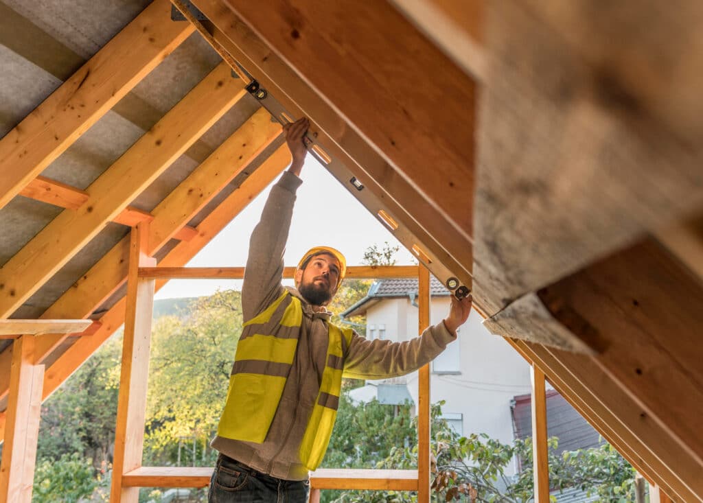 Un ouvrier portant un gilet et un casque de couleur jaune, fixant la toiture d'une maison en bois.